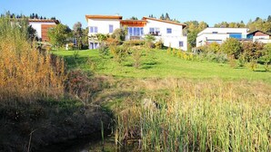 Ein modernes Haus mit weißer Fassade und orangefarbenem Dach, umgeben von einer Rasenfläche und einem kleinen Teich.