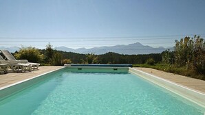 Ein rechteckiger Pool mit klarem Wasser, umgeben von Liegestühlen und Blick auf Berge.