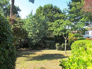 A garden with various trees and shrubs, a lawn, and a white building in the background.