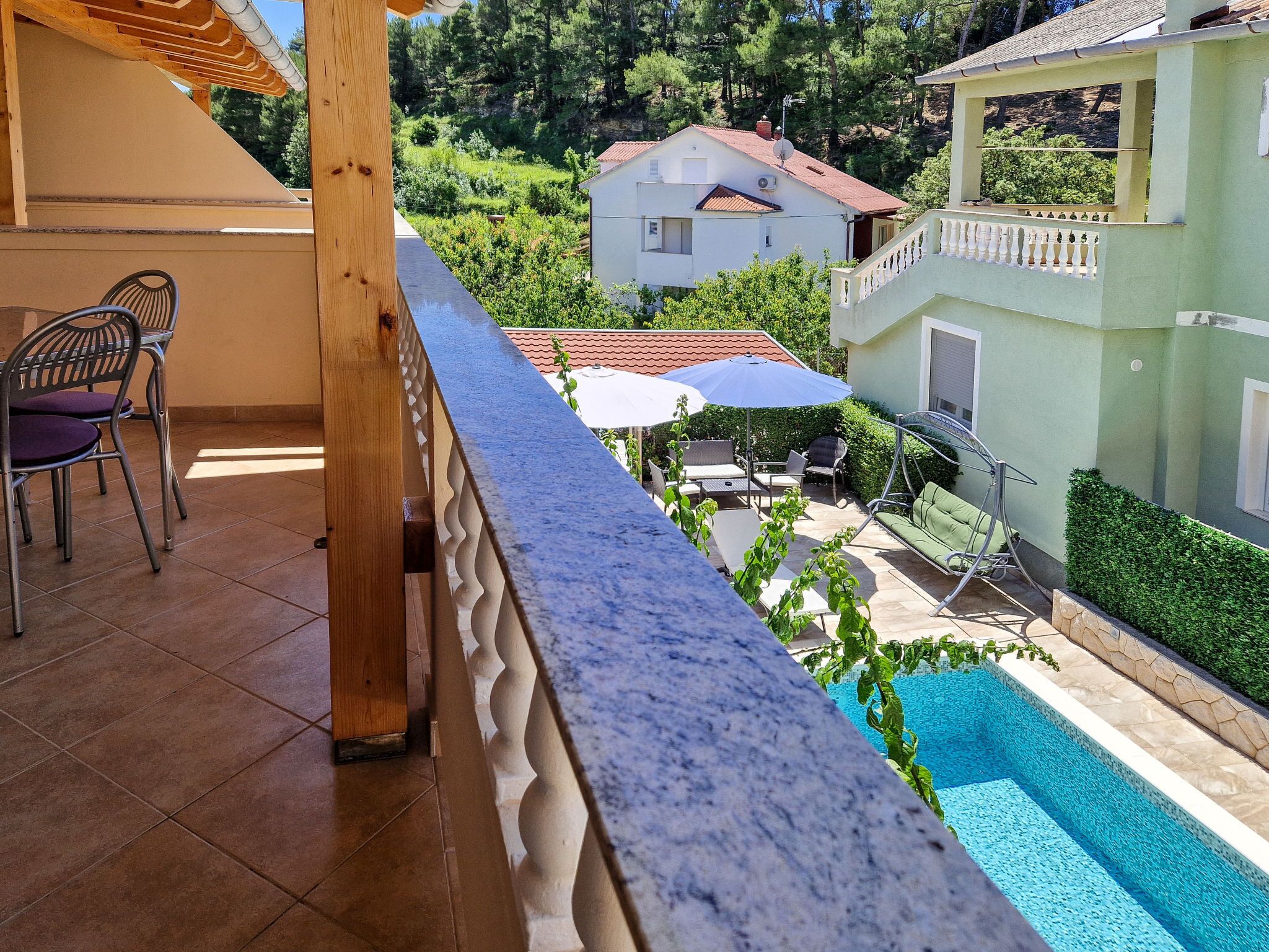 Un balcon donnant sur une piscine, une pergola en bois et un espace détente avec des chaises et une table.