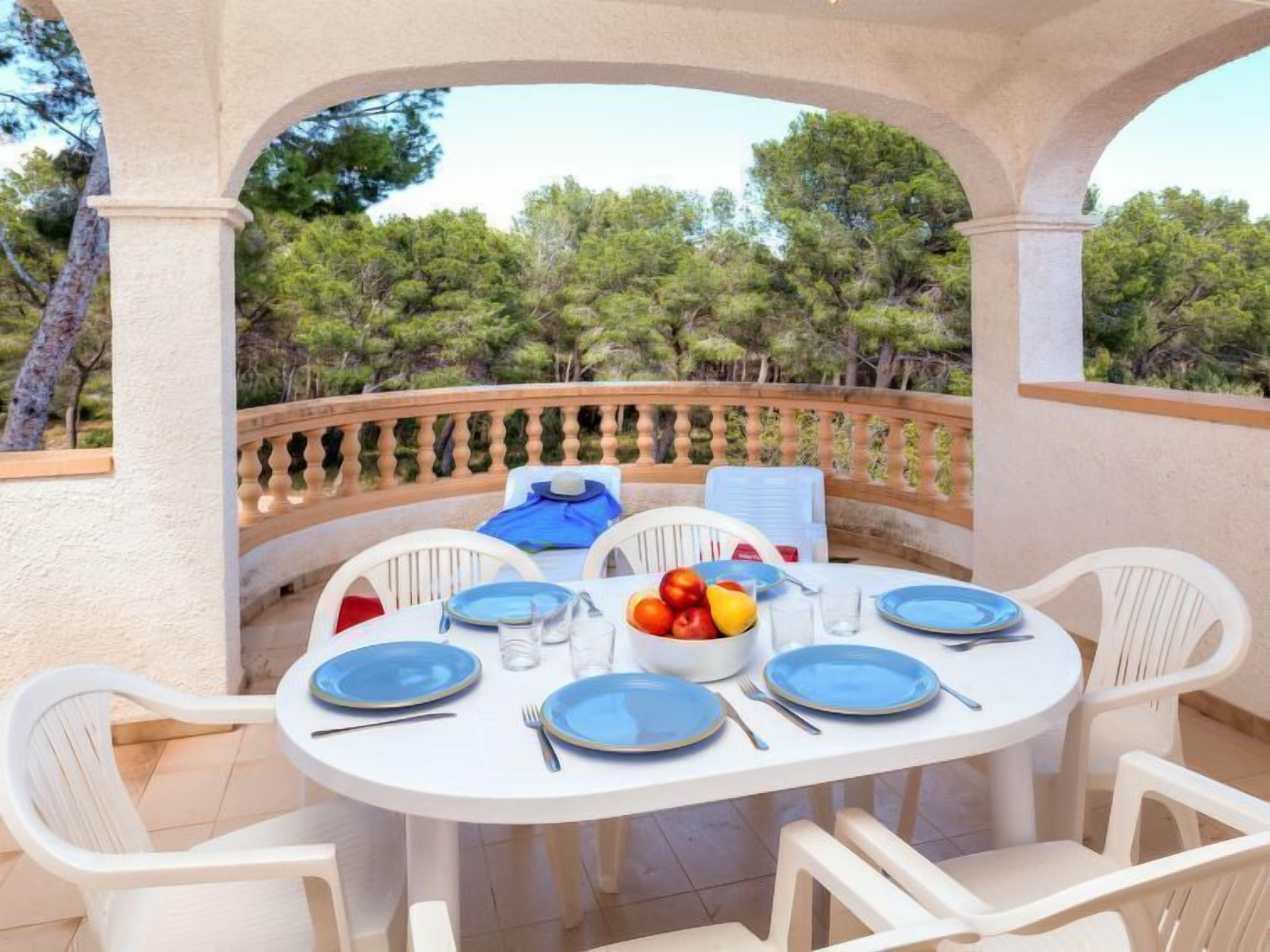 Een ronde tafel met blauwe borden, witte stoelen en een schaal met fruit.