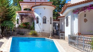 A Mediterranean-style villa with a swimming pool, terracotta roof tiles, and a garden with flowering plants.