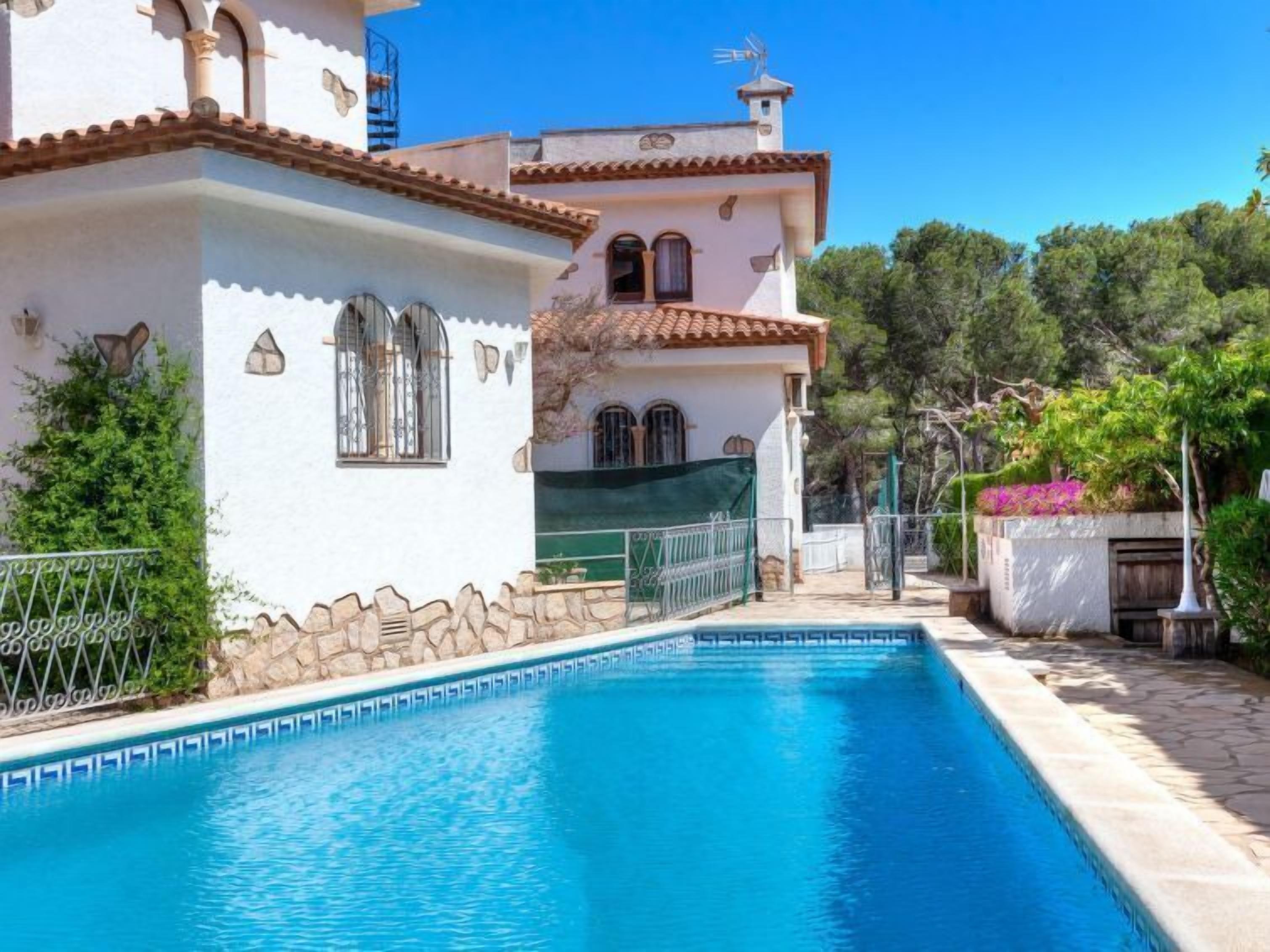 A swimming pool area with a white building, stone walls, and a tiled roof.