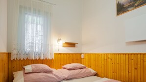 A room with two beds, a window with lace curtains, a wall-mounted light, and a painting. - Piccola by Interhome (Balatonakali)