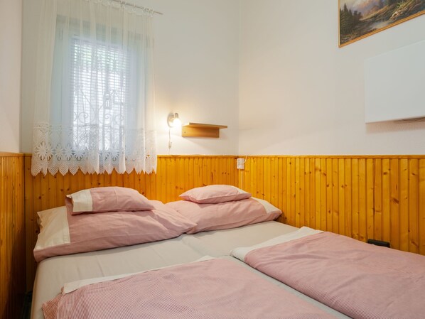 A room with two beds, a window with lace curtains, a wall-mounted light, and a painting.