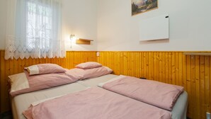 Un dormitori amb dos llits, una finestra amb cortines de galeria, una làmpada penjada a la paret i un quadre.