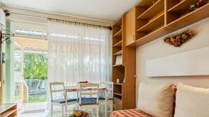 A living room with a checkered sofa, a coffee table with a remote control, and a dining area with chairs and a table. - Piccola by Interhome (Balatonakali)