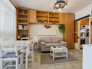A compact living space with a sofa, dining table, chairs, a small kitchen area, and a decorative wall piece. - Piccola by Interhome (Balatonakali)