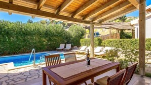 A wooden pergola with a pool table and chairs, surrounded by lush greenery and a clear blue pool. - Mihaela 2 by Interhome (Rab/Rab)