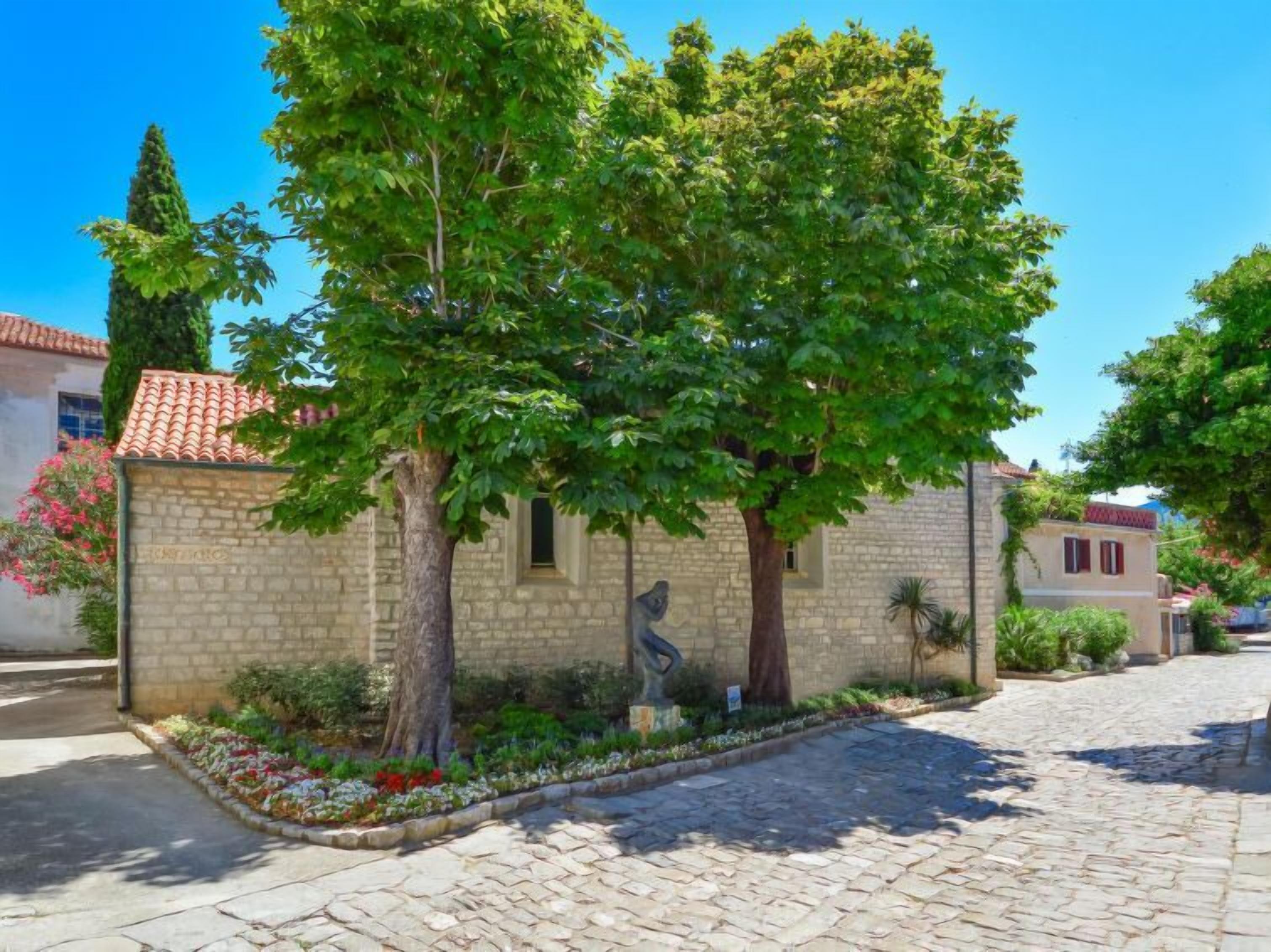 A stone building with a tiled roof, surrounded by cobblestone pavement and lush greenery.