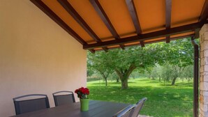 Une terrasse extérieure avec une table et des chaises, une pergola au-dessus et une vue sur un espace verdoyant avec des arbres.