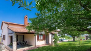 Une maison à deux étages, avec un toit en tuiles, une cheminée et un patio couvert aménagé avec du mobilier d’extérieur.