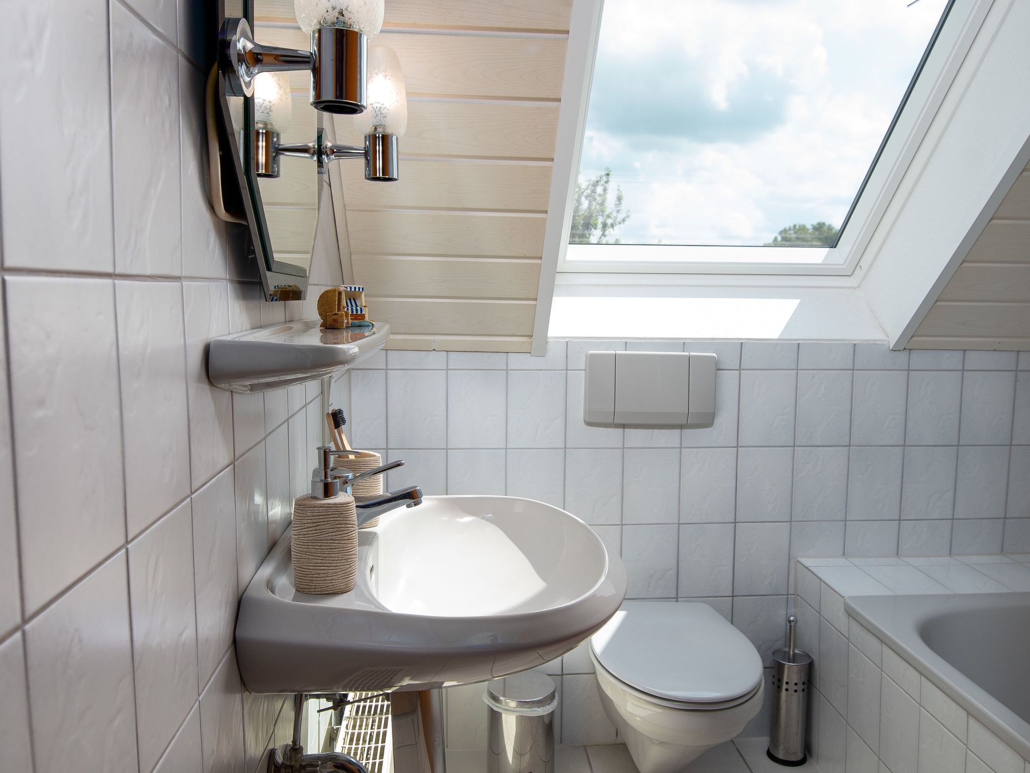 A modern bathroom with a skylight, white tiles, a sink, a toilet, and a bathtub.