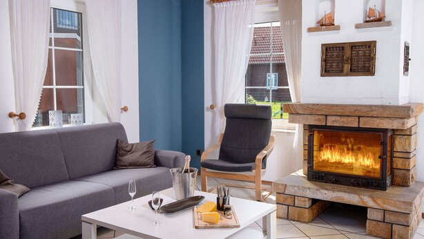 A living room with a fireplace, a sofa, a chair, and a table with glasses and a bottle. - Riedehuus by Interhome (Norddeich)