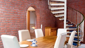 A dining area with a brick wall, a wooden table, white chairs, and a spiral staircase. - Riedehuus by Interhome (Norddeich)