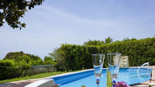 A poolside setting with two glasses of water, a hat, and a table with greenery.
