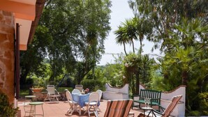 An outdoor patio with tables and chairs, surrounded by lush greenery and trees.