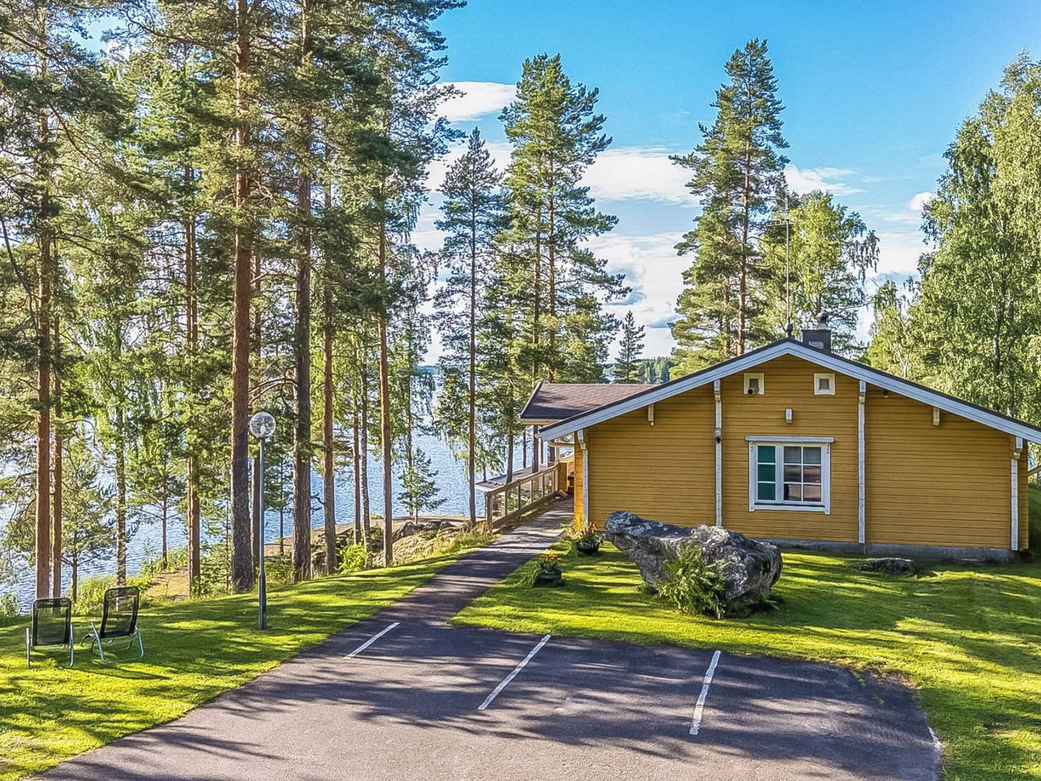 A lodge with a wooden exterior, a paved driveway, and a view of a lake surrounded by tall trees.