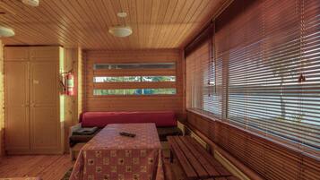 Interior de una cabaña con techo de madera, una mesa con mantel a cuadros, un banco y una ventana con persianas.