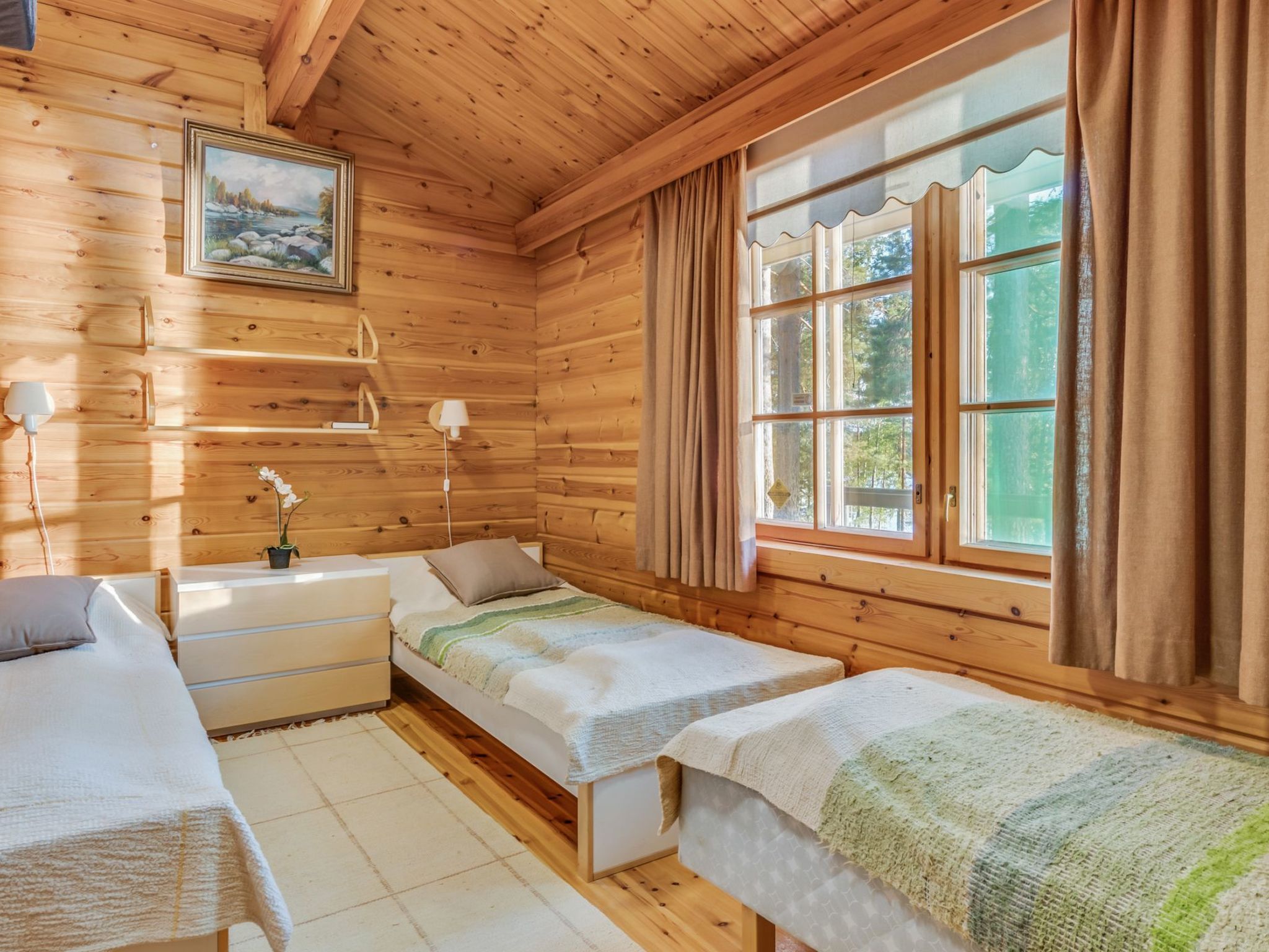 A cabin with two single beds, a wooden ceiling, a painting on the wall, and a window with curtains.