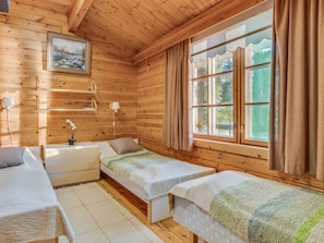 Una cabaña con dos camas individuales, techo de madera, un cuadro en la pared y una ventana con cortinas.
