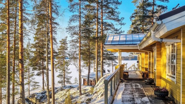 Une cabane en bois dotée d’un porche abrité, entourée de grands pins et d’un paysage enneigé.