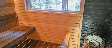 En stuga med träpanel på insidan, en bänk, ett fönster med utsikt över träd och en vägg av sten.