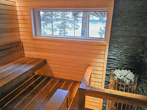 Ein Holzblockbau-Innenraum mit einer Bank, einem Fenster mit Blick auf Bäume und einer Steinwand.