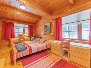 Een knus houten slaapkamer met een bed, bureau, stoel en grote ramen.