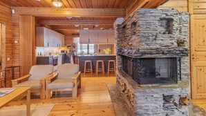 Un intérieur de chalet chaleureux avec une cheminée en pierre, des meubles en bois et un coin cuisine.