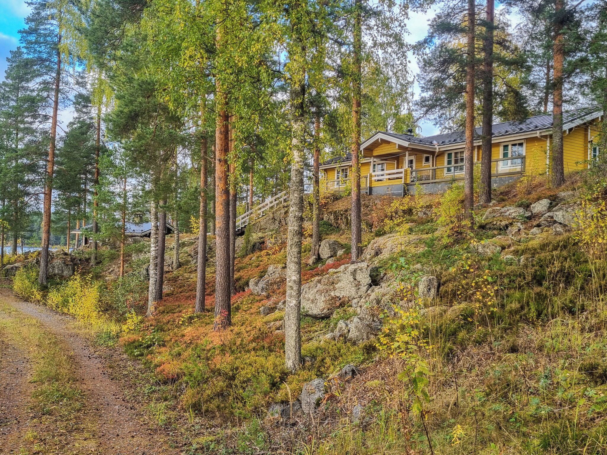 En gul stuga med en veranda, omgiven av höga tallar och ett bergigt landskap.