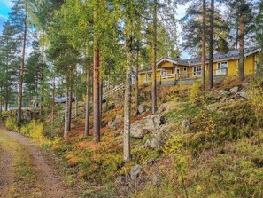 En gul stuga med en veranda, omgiven av höga tallar och ett bergigt landskap.