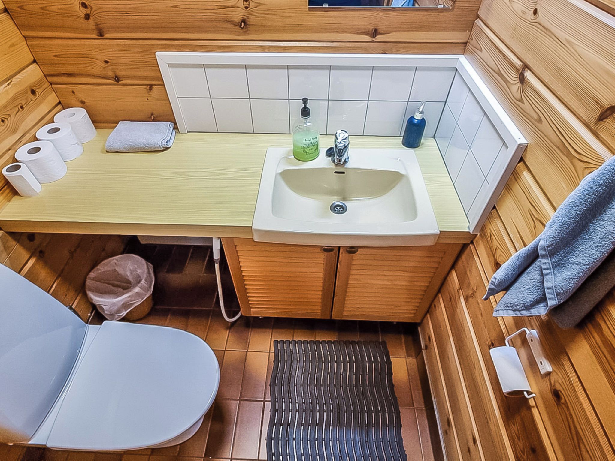 Un baño pequeño de madera con lavamanos, inodoro y zona de ducha.