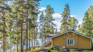 Un chalet avec une façade en bois, une allée pavée et une vue sur un lac entouré de grands arbres.
