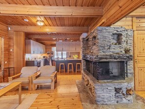 A cozy cabin interior with a stone fireplace, wooden furniture, and a kitchen area.