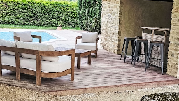 Eine Holzterrasse mit Sitzgelegenheiten im Freien, einem Pool und einem Steinhaus mit Barbereich.