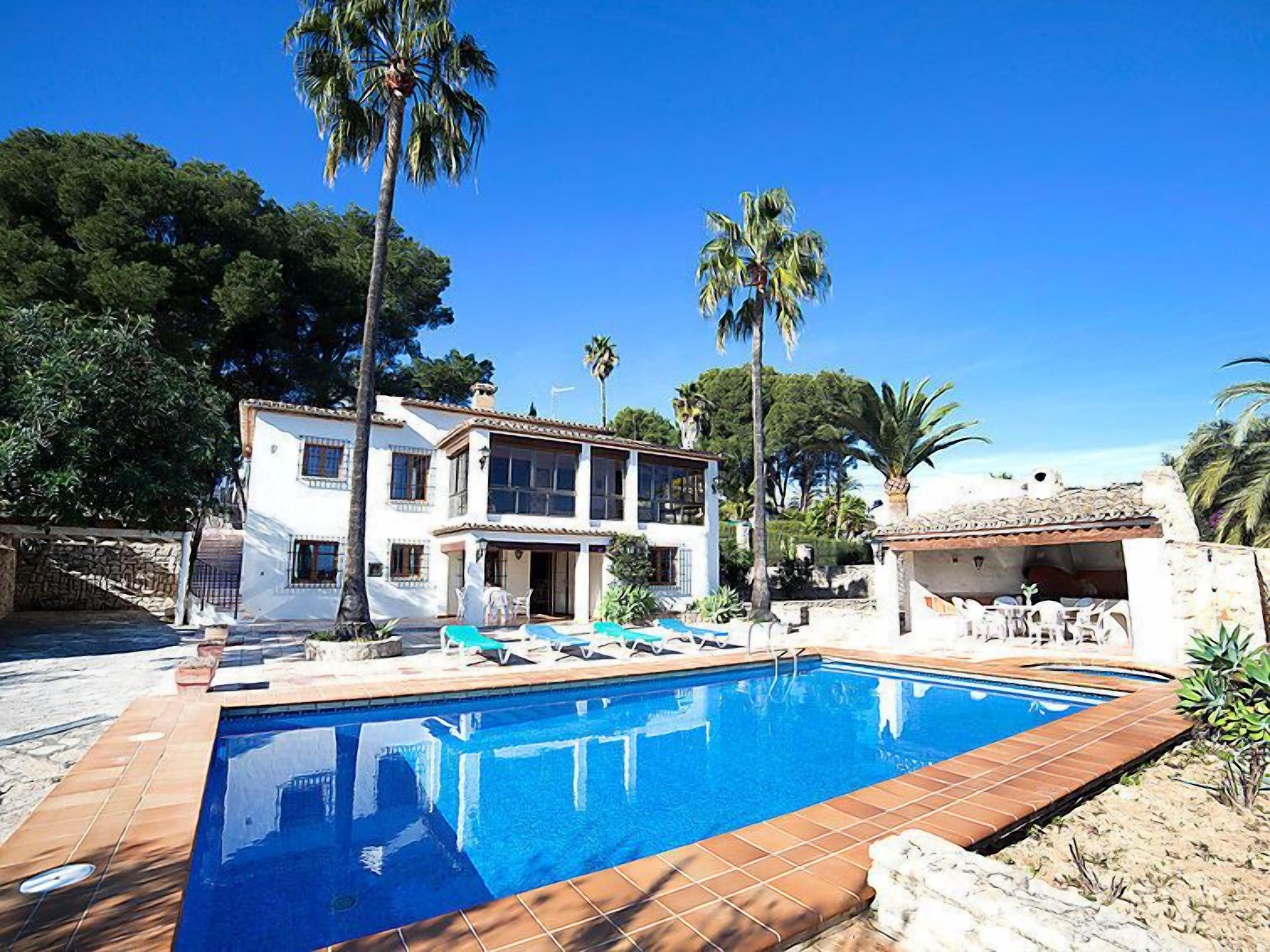 A two-story house with a swimming pool, surrounded by palm trees and a clear blue sky.