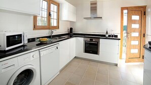 A modern kitchen with white cabinets, a Bosch dishwasher, a microwave, a stove, and a window with wooden frames. - Els Pins by Interhome (Calpe/Calp)