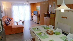 Een moderne woonkamer met een bank, een eettafel gedekt voor twee personen en een keuken op de achtergrond.