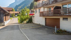 Een modern gebouw met een parkeerplaats, een rode auto ervoor geparkeerd en een uitzicht op een berg in de verte.