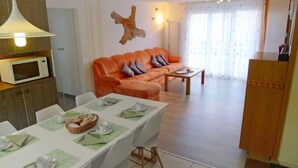Een moderne woonkamer met een bank, een eettafel voor twee personen en een keuken met een magnetron.