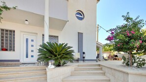 A building with a white facade, a large potted plant, and a staircase leading to a door with a window. - Apartment Anđa by Interhome (Trogir/Slatine)