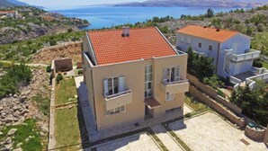 A modern two-story house with a red-tiled roof, situated on a hillside with a view of a large body of water and mountains in the distance. - Apartment Golub by Interhome (Karlobag)