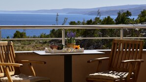 A balcony with two wooden chairs, a small table, and a view of the sea and hills. - Apartment Golub by Interhome (Karlobag)