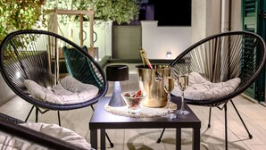 En terrasse med to sorte fletstole, et lille bord, en flaske champagne og to glas.