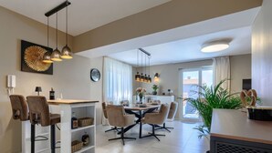 Et moderne køkken med spiseplads, med et stort vindue, en lysekrone og et ur på væggen.