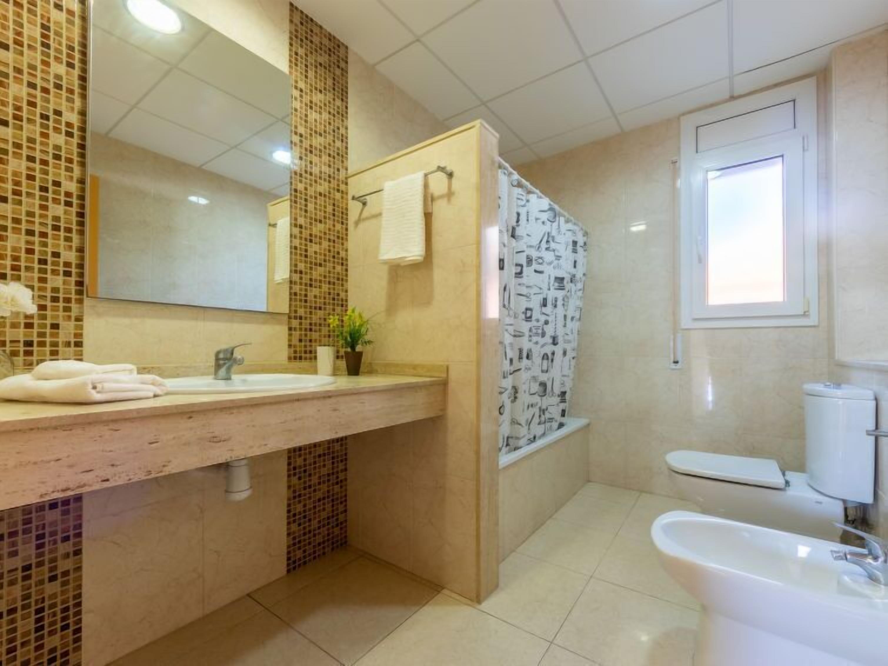 Un baño con un espejo grande, un lavabo, un inodoro y una bañera.