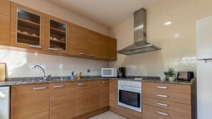 A modern kitchen with wooden cabinets, a stainless steel range hood, a microwave, and an oven. - Vacation home Alex by Interhome (Deltebre)