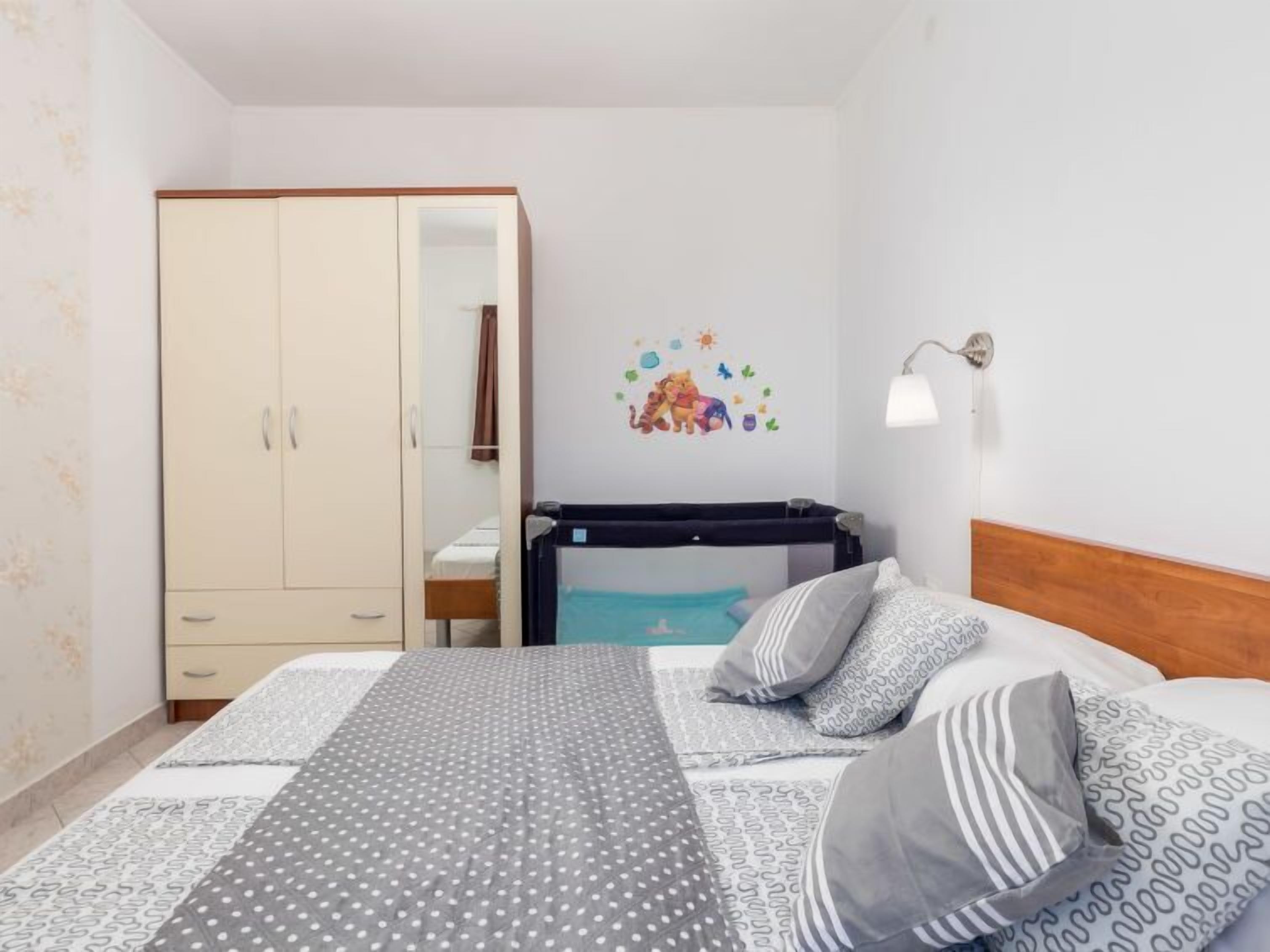 Une chambre à coucher comprenant un lit, une armoire, un berceau et un élément décoratif mural.