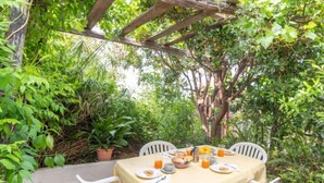 Un espace de restauration en plein air avec une table dressée pour deux personnes, entouré d’une végétation luxuriante et surmonté d’une pergola.